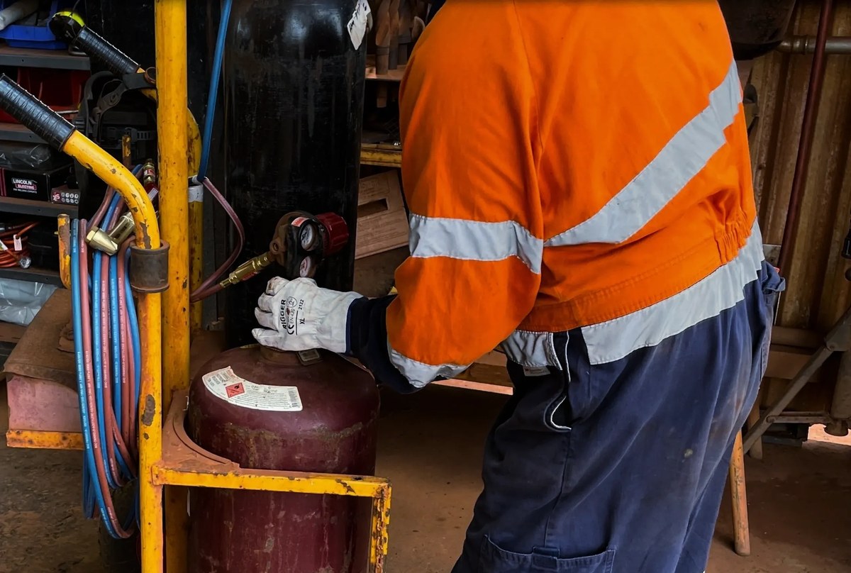 Worker in hi vis handling a heavy gas cylinder in a workshop